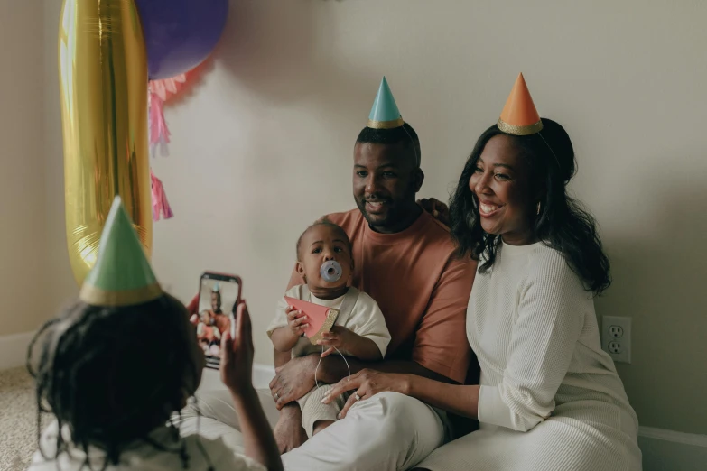 a man and woman taking a picture of a baby, a portrait, by Carey Morris, pexels contest winner, happening, party hats, photo of a black woman, promotional image, celebrating a birthday