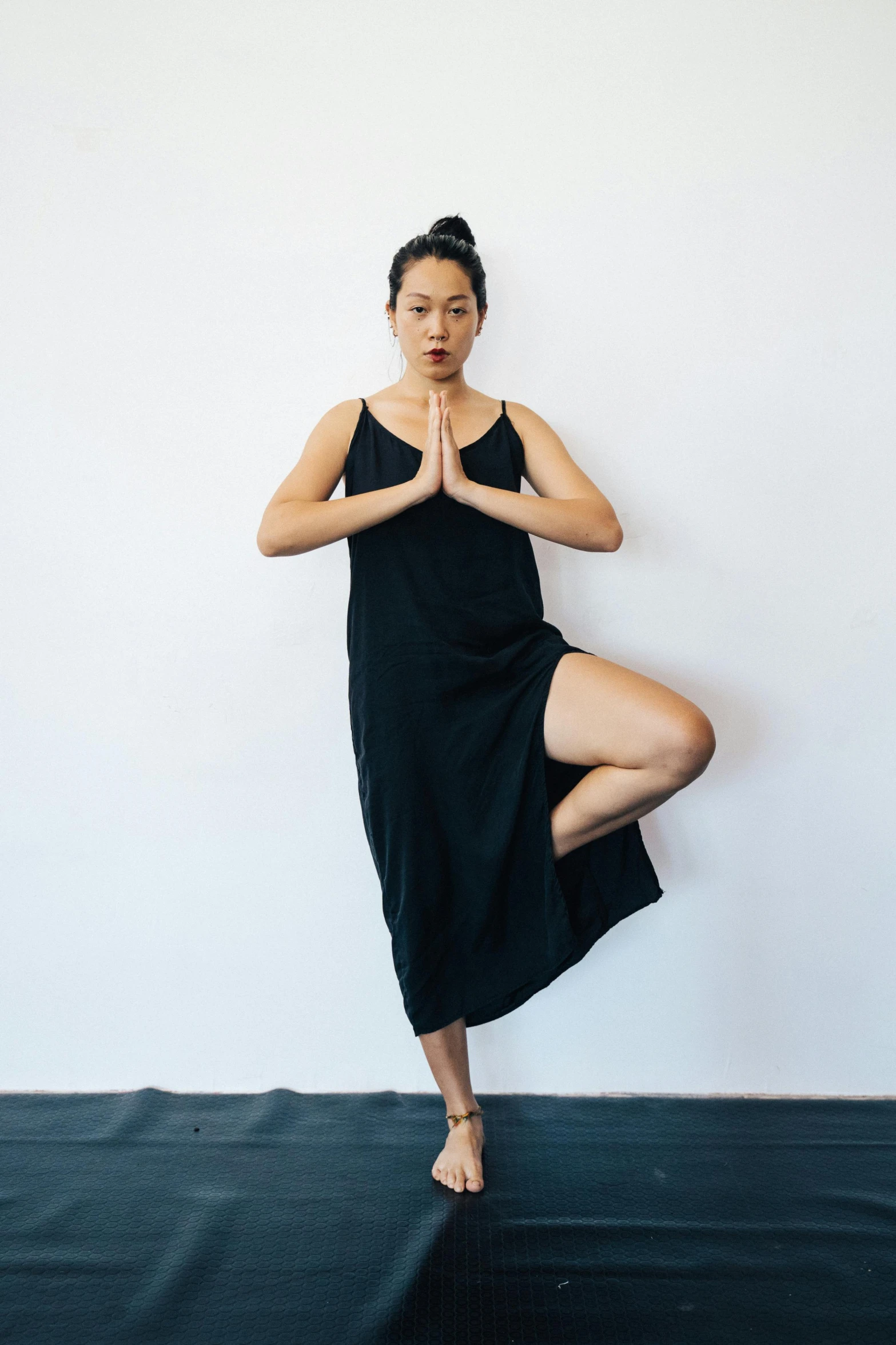 a woman in a black dress doing a yoga pose, inspired by Li Di, happening, curated collections, south east asian with long, shows a leg, organic dress