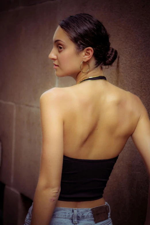 a woman standing in front of a wall with her back to the camera, flickr, black halter top, slicked-back hair, middle eastern skin, over-the-shoulder-shot