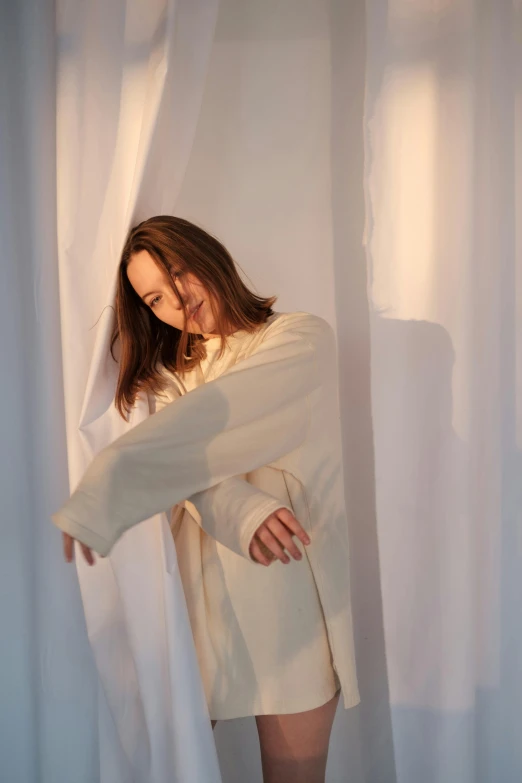 a woman standing in front of a white curtain, an album cover, inspired by Anna Füssli, unsplash, wearing a duster coat, frank dillane, distorted pose, studio backlight