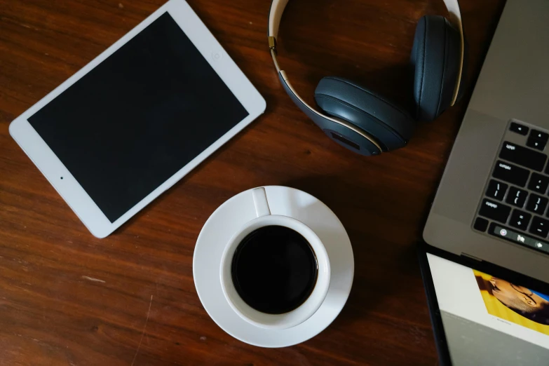 a laptop computer sitting on top of a wooden table next to a cup of coffee, wearing black headphones, thumbnail, diverse, the