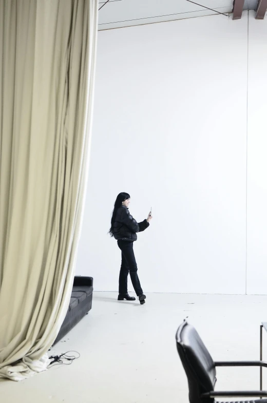 a woman standing in front of a white backdrop, inspired by Fei Danxu, unsplash, visual art, checking her phone, with long black hair, inside a tall vetical room, fully covered in drapes