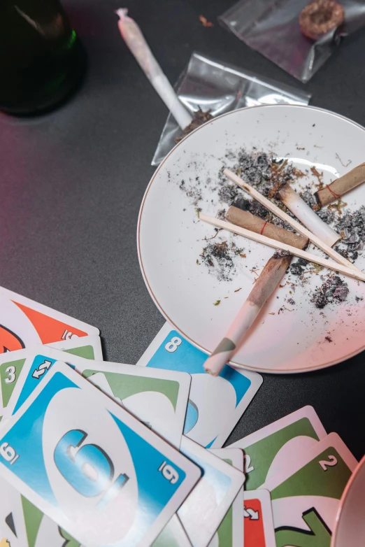 a white plate topped with cigarettes and playing cards, by Julia Pishtar, process art, smoking a bowl of hash together, promo image, thrown tables, colors