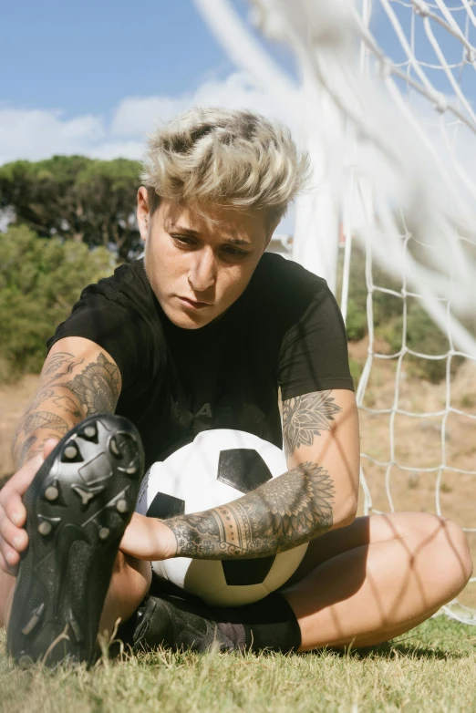 a man kneeling on the ground with a soccer ball, a tattoo, trending on pexels, portrait androgynous girl, short platinum hair tomboy, video still, photograph of a sleeve tattoo