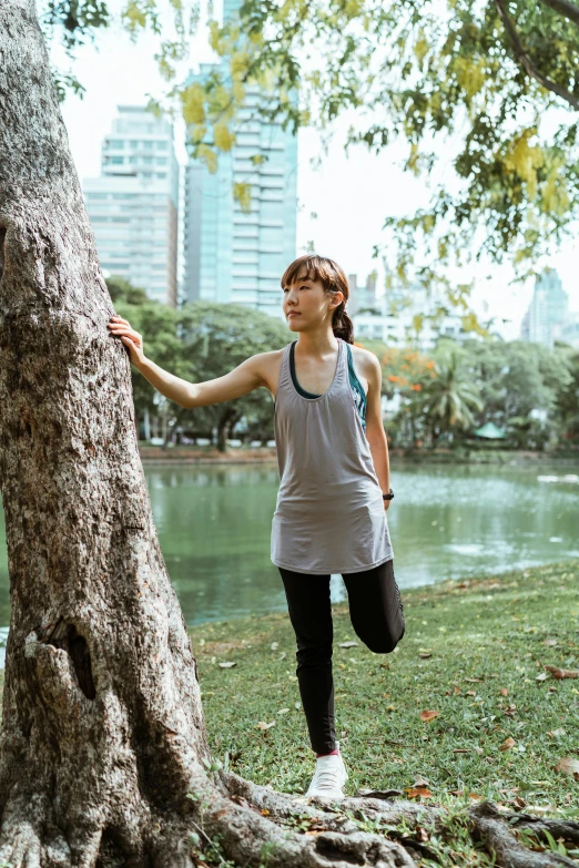 a woman standing next to a tree in a park, inspired by Ruth Jên, happening, standing athletic pose, bangkok, 5k, near pond