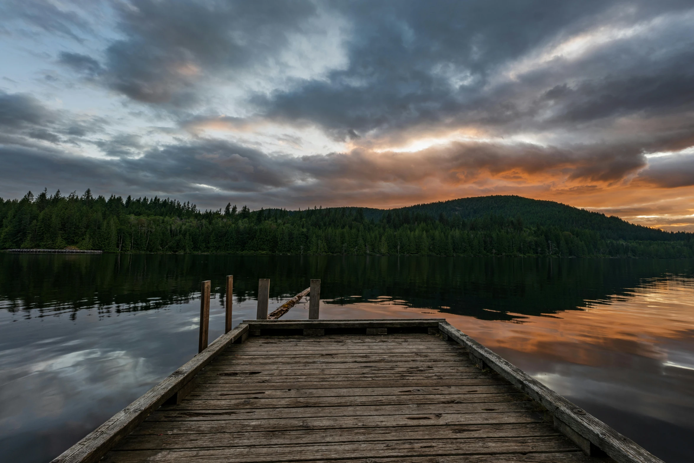 a dock sitting on top of a lake under a cloudy sky, by Jessie Algie, pexels contest winner, boreal forest, sunset light, british columbia, fire lit