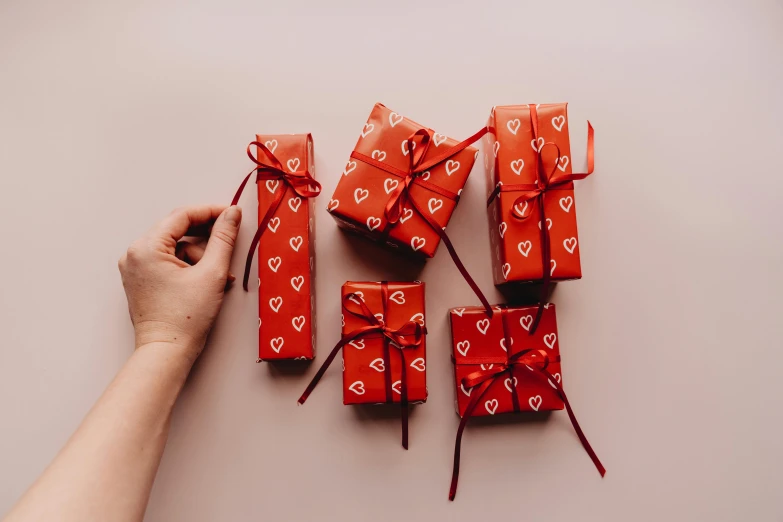 a person holding a bunch of wrapped presents, by Sylvia Wishart, pexels contest winner, red theme, packaging design, red hearts, on a pale background