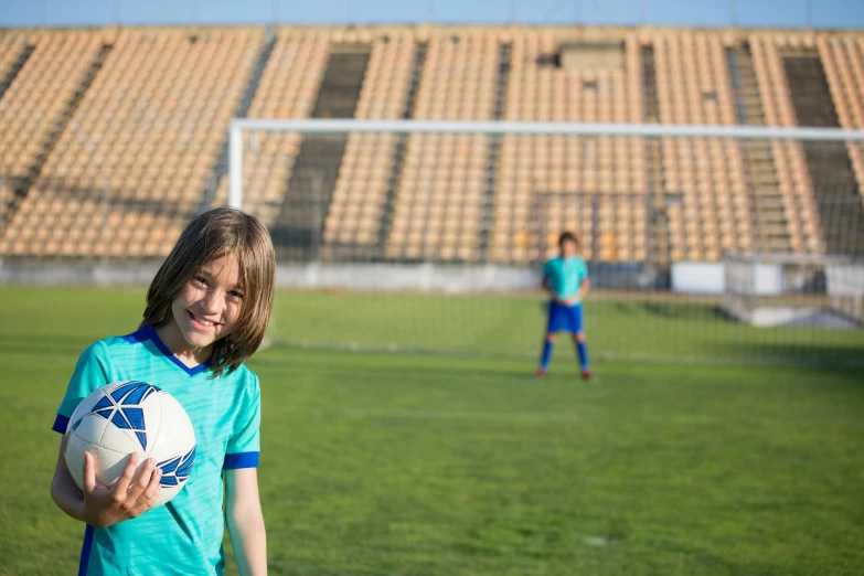 a young girl holding a soccer ball on a soccer field, pexels contest winner, in egypt, avatar image, looking to camera, ad image