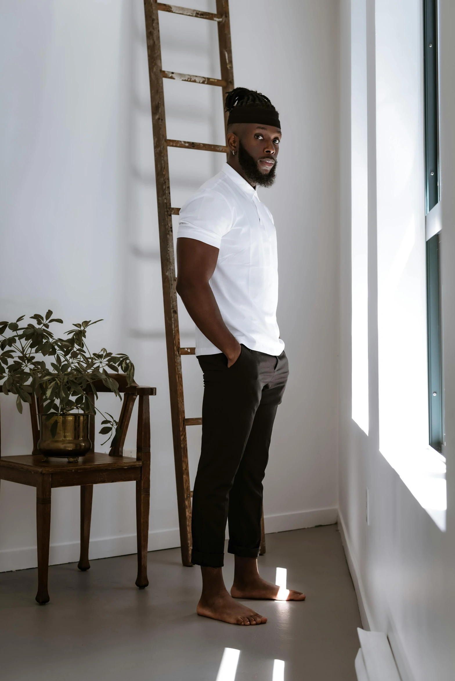 a man standing next to a ladder in a room, inspired by Theo Constanté, pexels contest winner, wearing polo shirt, ( ( dark skin ) ), brown pants, on a white table