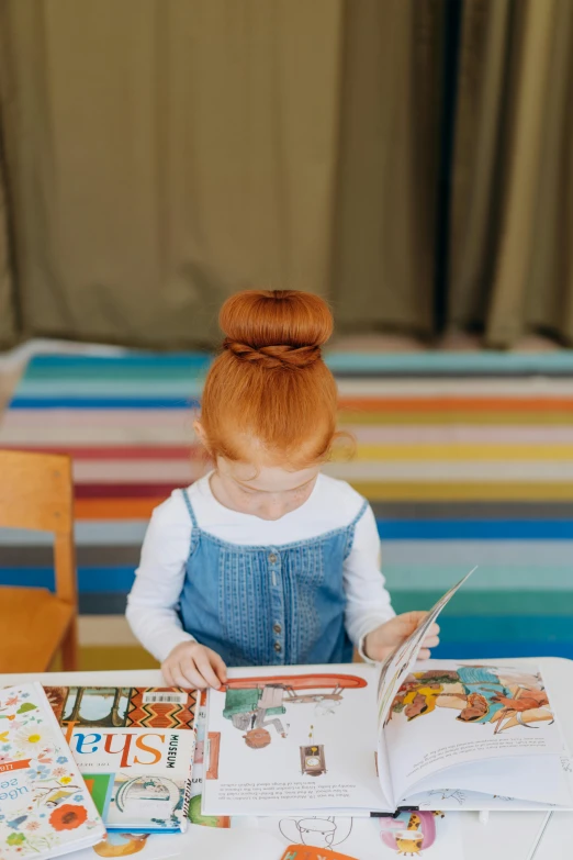 a little girl sitting at a table reading a book, inspired by Elsa Beskow, pexels contest winner, orange hair bow, gif, topknot, ( redhead