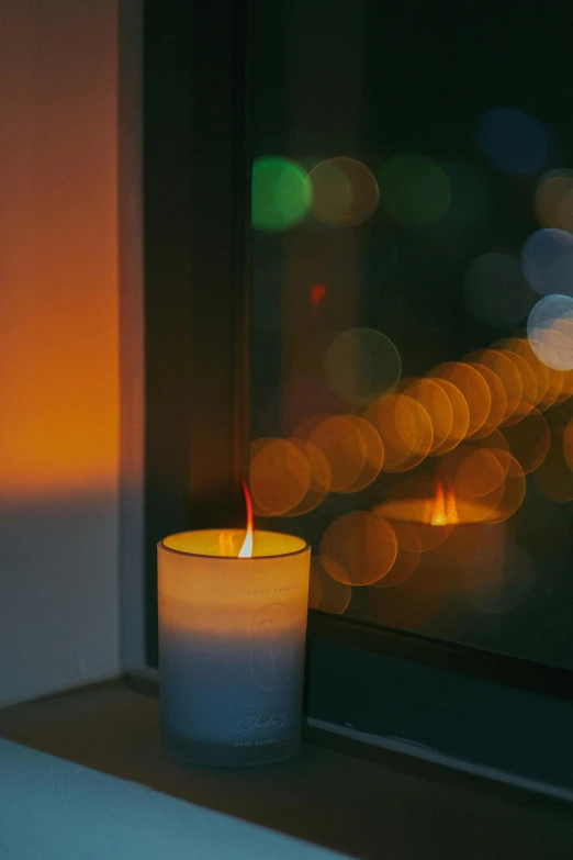 a lit candle sitting on top of a window sill, inspired by Elsa Bleda, unsplash, light and space, made of glowing wax, city lights, light orange mist, reflected light