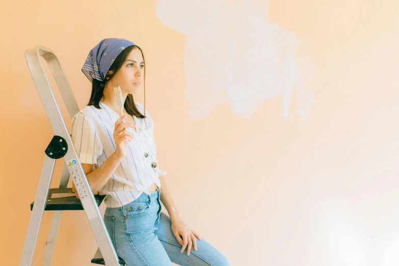 a woman sitting on top of a ladder, a painting, trending on pexels, pastel clothing, wall painting, wearing denim, pale orange colors