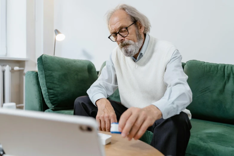 a man sitting on a couch in front of a laptop, by Will Ellis, trending on pexels, balding older cyborg repairing, white reading glasses, old gigachad with grey beard, casual game