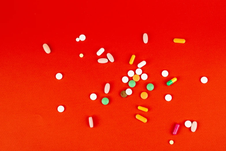 a bunch of pills on a red surface, by Julia Pishtar, pexels, antipodeans, colored dots, red and orange colored, surgical impliments, micro - organisms