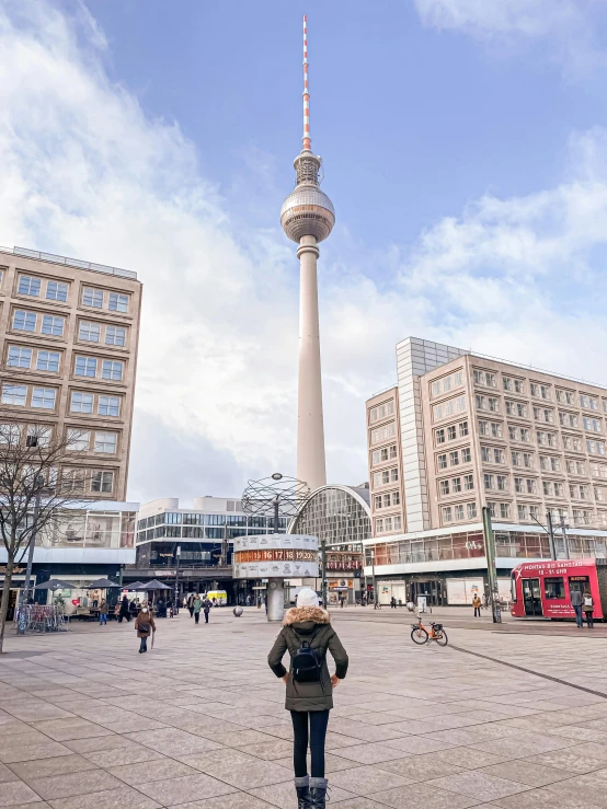 a woman standing in front of a tall tower, pexels contest winner, berlin secession, 🚿🗝📝, fresh bakeries in the background, entertainment district, panorama