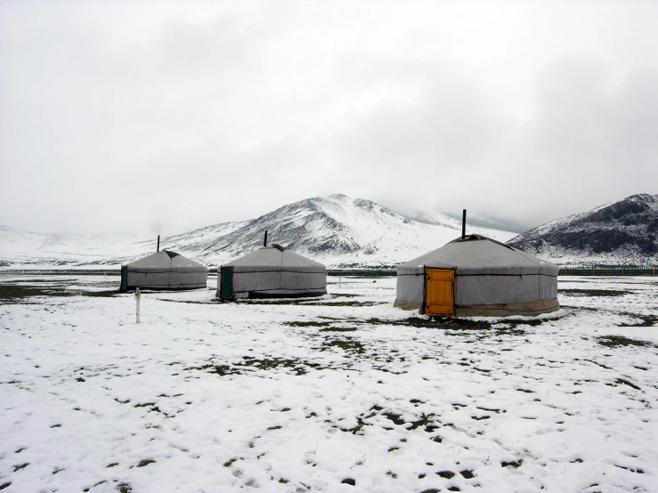 a group of yurts sitting on top of a snow covered field, grey skies, conde nast traveler photo