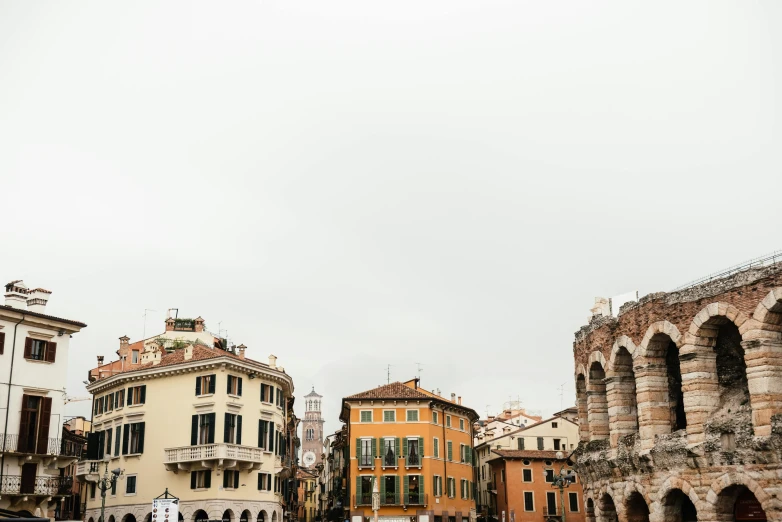 a group of people walking down a street next to tall buildings, inspired by Canaletto, pexels contest winner, neoclassicism, coliseum, overcast gray skies, italian looking emma, square