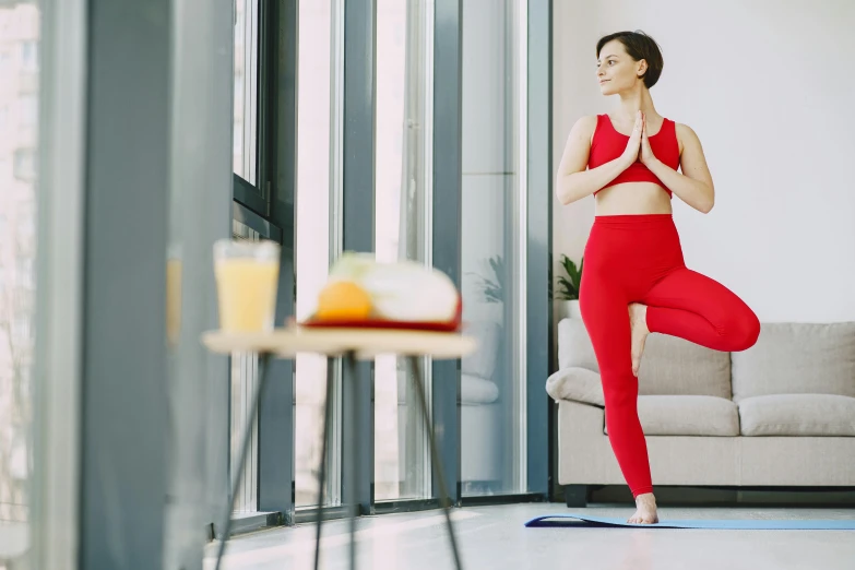 a woman doing a yoga pose in a living room, pexels contest winner, arabesque, red suit, standing confidently, al fresco, manuka