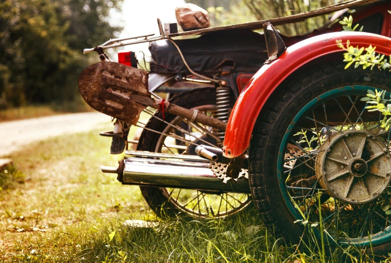 a red motorcycle parked on top of a lush green field, vintage car, historically accurate, stuck in mud, retro colour