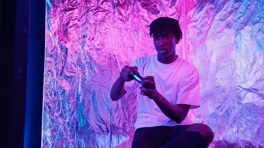 a man sitting on a stool holding a cell phone, pexels contest winner, afrofuturism, purple and pink and blue neons, gaming room, black teenage boy, holding controller