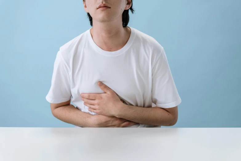 a man sitting at a table with his hands on his chest, trending on pexels, square, with organs, wearing crop top, cysts