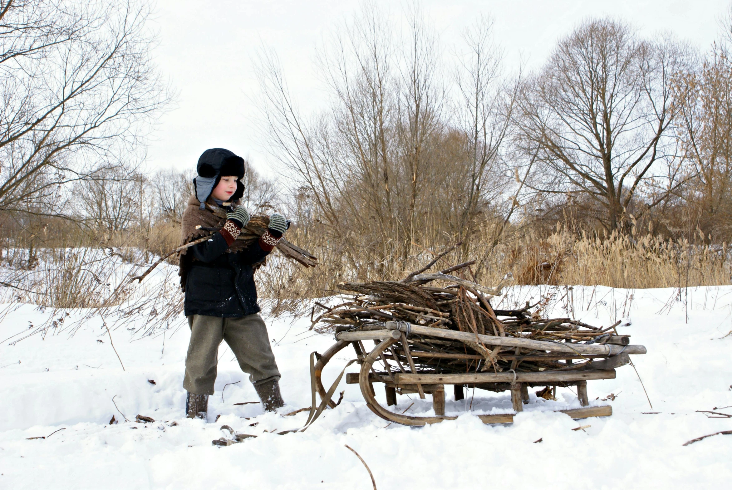 a man standing next to a pile of wood in the snow, an album cover, inspired by Vladimir Borovikovsky, flickr, toddler, holding flamethrower, ukraine. photography, historically accurate