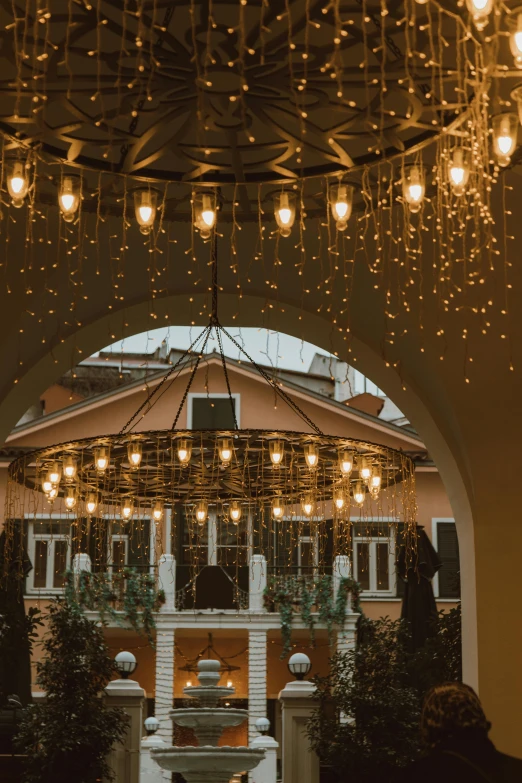 a bride and groom standing under a chandelier, inspired by Riad Beyrouti, pexels contest winner, art nouveau, patio, christmas lights, symmetrical image, brown