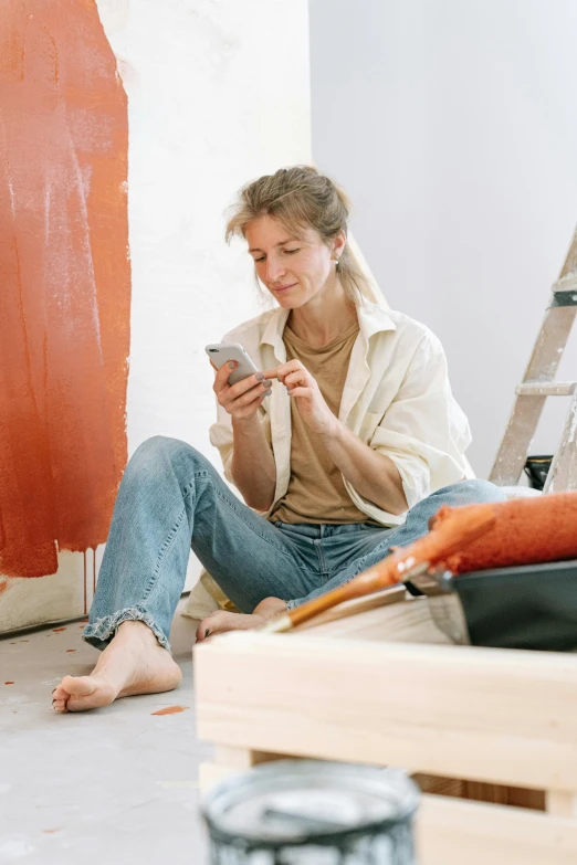 a woman sitting on the floor using a cell phone, a painting, trending on pexels, arbeitsrat für kunst, gray and orange colours, maintenance photo, looking happy, profile image