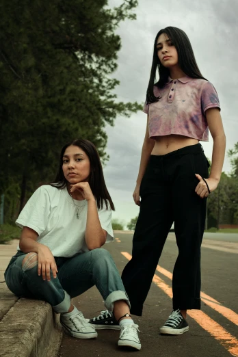 two women sitting on the side of a road, an album cover, trending on pexels, wearing polo shirt, standing, hot topic, hispanic