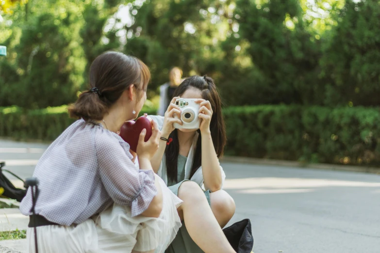 a couple of women sitting next to each other on a sidewalk, a picture, pexels contest winner, holding polaroid camera, asian women, youtube thumbnail, half image