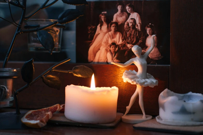 a candle sitting on top of a table next to a picture, a statue, pexels contest winner, ballet dancer, miniatures, vintage photograph, made of glowing wax and ceramic