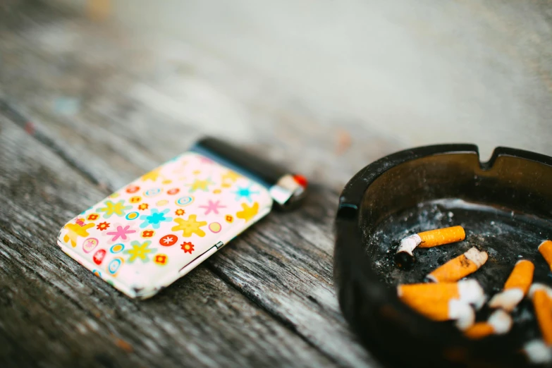 a cigarette case sitting on top of a wooden table, a still life, by Julia Pishtar, trending on pexels, graffiti, s'mores, phone photo, multicoloured, floral patterned skin