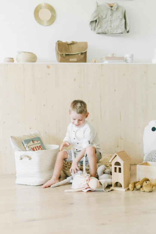 a little boy that is sitting on the floor, by Eden Box, inside a child's bedroom, natural materials, bags, in a white boho style studio