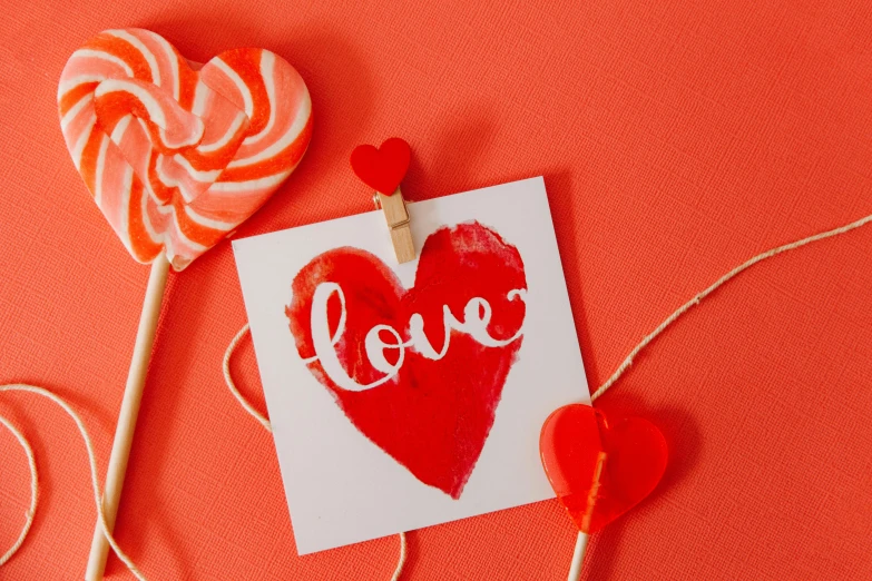 two lollipops and a card with the word love written on it, a picture, by Julia Pishtar, trending on pexels, coral red, red paint detail, heart, full product shot