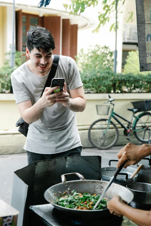 a group of people standing around a table with food on it, on a street, selfie of a man, cooking it up, lachlan bailey