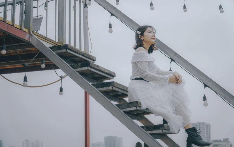 a woman in a white dress sitting on a set of stairs, inspired by Cheng Jiasui, pexels contest winner, cafe in the clouds, grey, music video, kotegawa yui