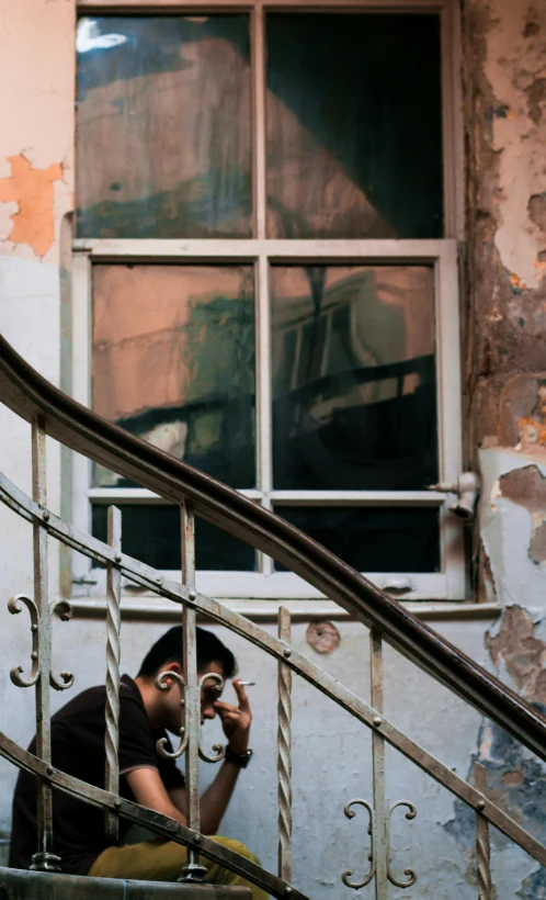 a man sitting on a set of stairs talking on a cell phone, a photo, by Ihor Podolchak, broken windows, colour photograph, photographed for reuters, demur