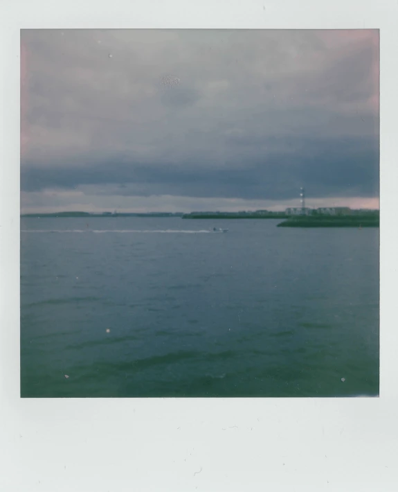 a large body of water with a lighthouse in the distance, a polaroid photo, helsinki, long distance photo, muted coloures, slightly blurry