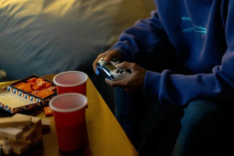 a person sitting on a couch playing a video game, inspired by Elsa Bleda, pexels, hyperrealism, a table full of candy, awkwardly holding red solo cup, night setting, xbox series x