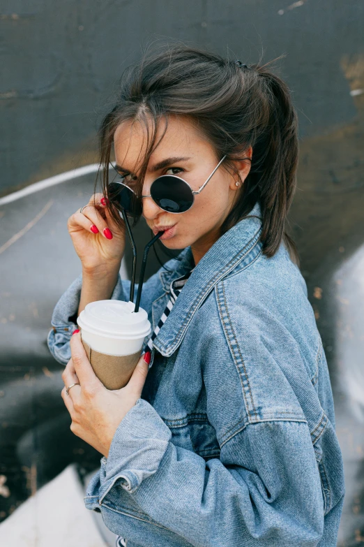 a woman in a denim jacket holding a cup of coffee, trending on pexels, implanted sunglasses, portrait sophie mudd, brunette hair, fashionista