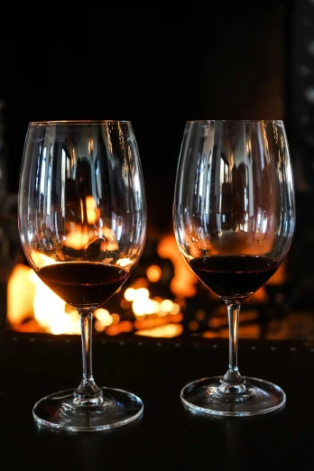 two wine glasses sitting next to each other on a table, fire place roaring, february), front and center, port