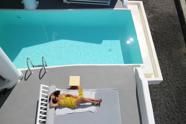 a woman laying on a bed next to a pool, santorini, square, grey, apartment