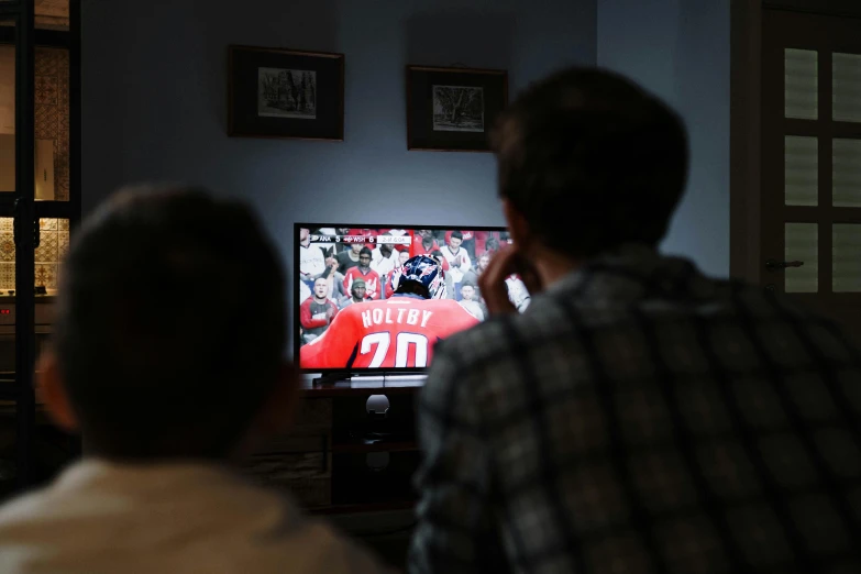 a couple of men sitting in front of a tv, by Adam Marczyński, pexels, nfl, facing away from camera, college, promo image