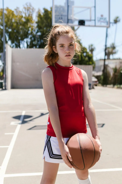 a young girl standing on a basketball court holding a basketball, by Gavin Hamilton, sadie sink, wearing red tank top, sleeveless turtleneck, wearing adidas clothing