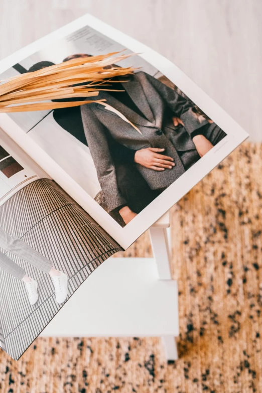 an open magazine sitting on top of a table, a picture, by Julia Pishtar, trending on unsplash, wearing white suit, natural materials, herringbone floor, fashion poster