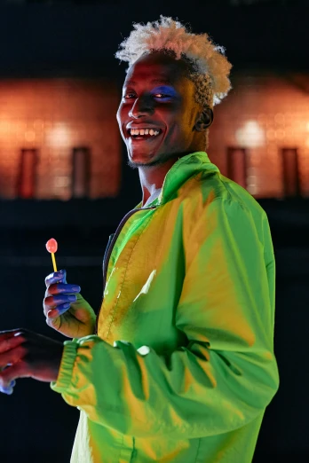 a man in a yellow jacket holding a toothbrush, by Ingrida Kadaka, trending on pexels, visual art, night clubs and neons, brown skin man with a giant grin, ru paul\'s drag race, neon paint drip