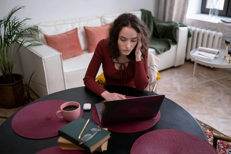 a woman sitting at a table with a laptop, crimson themed, struggling, sitting on a mocha-colored table, taken in 2 0 2 0