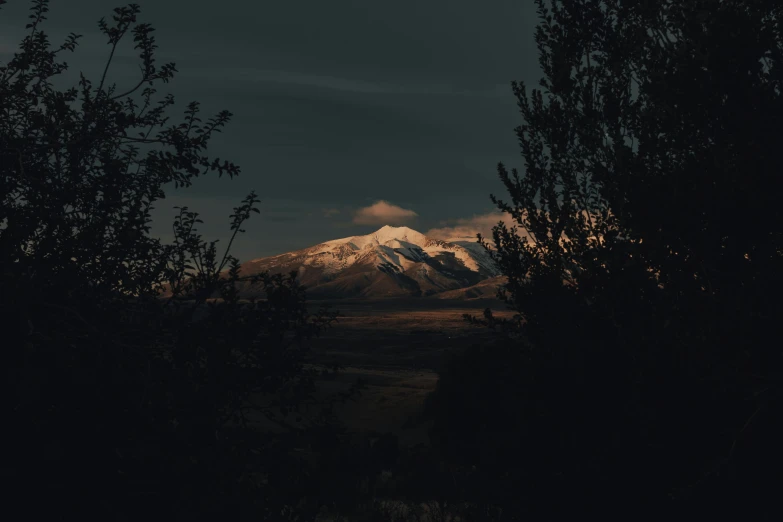 a mountain in the distance with trees in the foreground, inspired by Elsa Bleda, hurufiyya, low key light, dark volcano background, instagram picture, underexposed photography