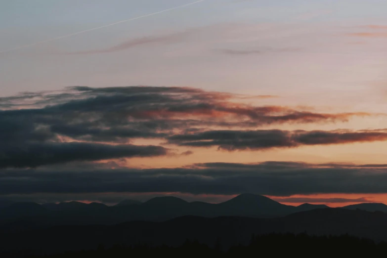 a person flying a kite at sunset with mountains in the background, by Emma Andijewska, pexels contest winner, panorama view of the sky, dark and muted colors, cloudy sunset, slightly pixelated