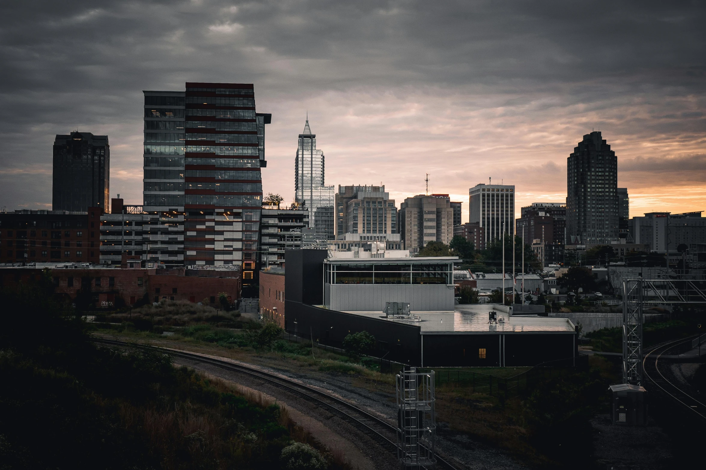 a train traveling through a city next to tall buildings, by Andrew Domachowski, unsplash contest winner, overcast dusk, realistic photo of a town, glass and steel, dark and forboding